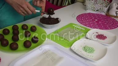 一个女人把海绵蛋糕上的球浸到巧克力里。 做一个土豆蛋糕。 盘子旁边有蛋糕、液体巧克力和